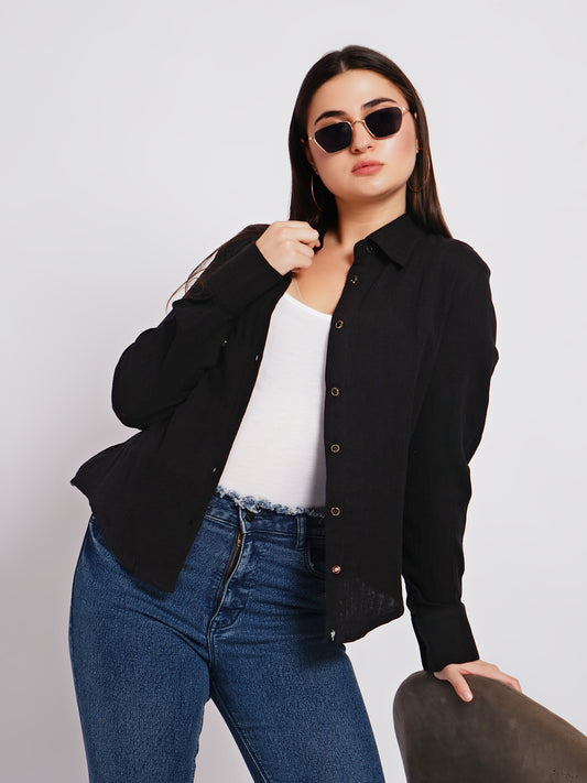 Woman wearing a black jacket, white shirt, and blue jeans against a plain background