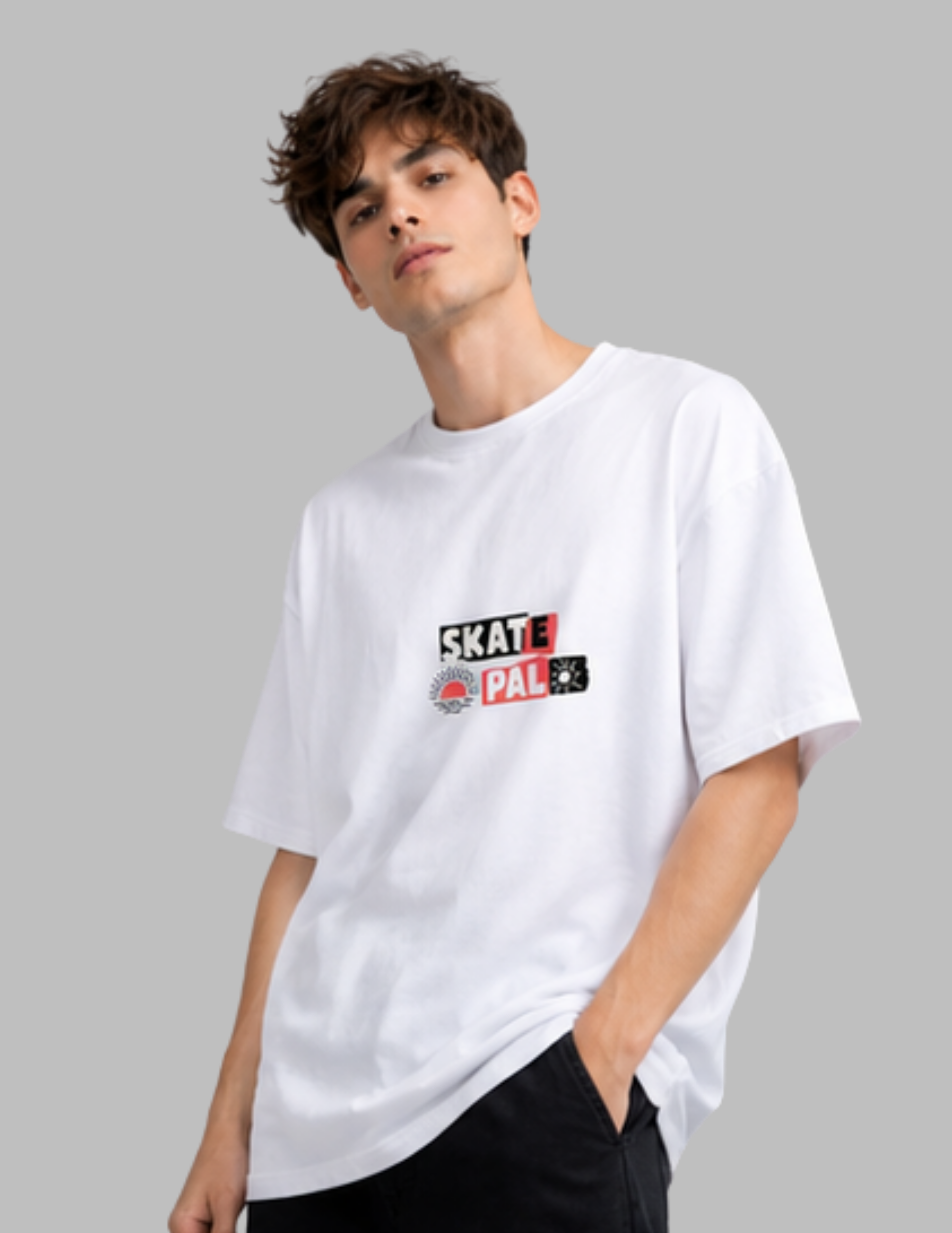 A young man wearing a white short-sleeve t-shirt with a 'Skate Pal' graphic on the chest, paired with black pants, set against a solid gray background.