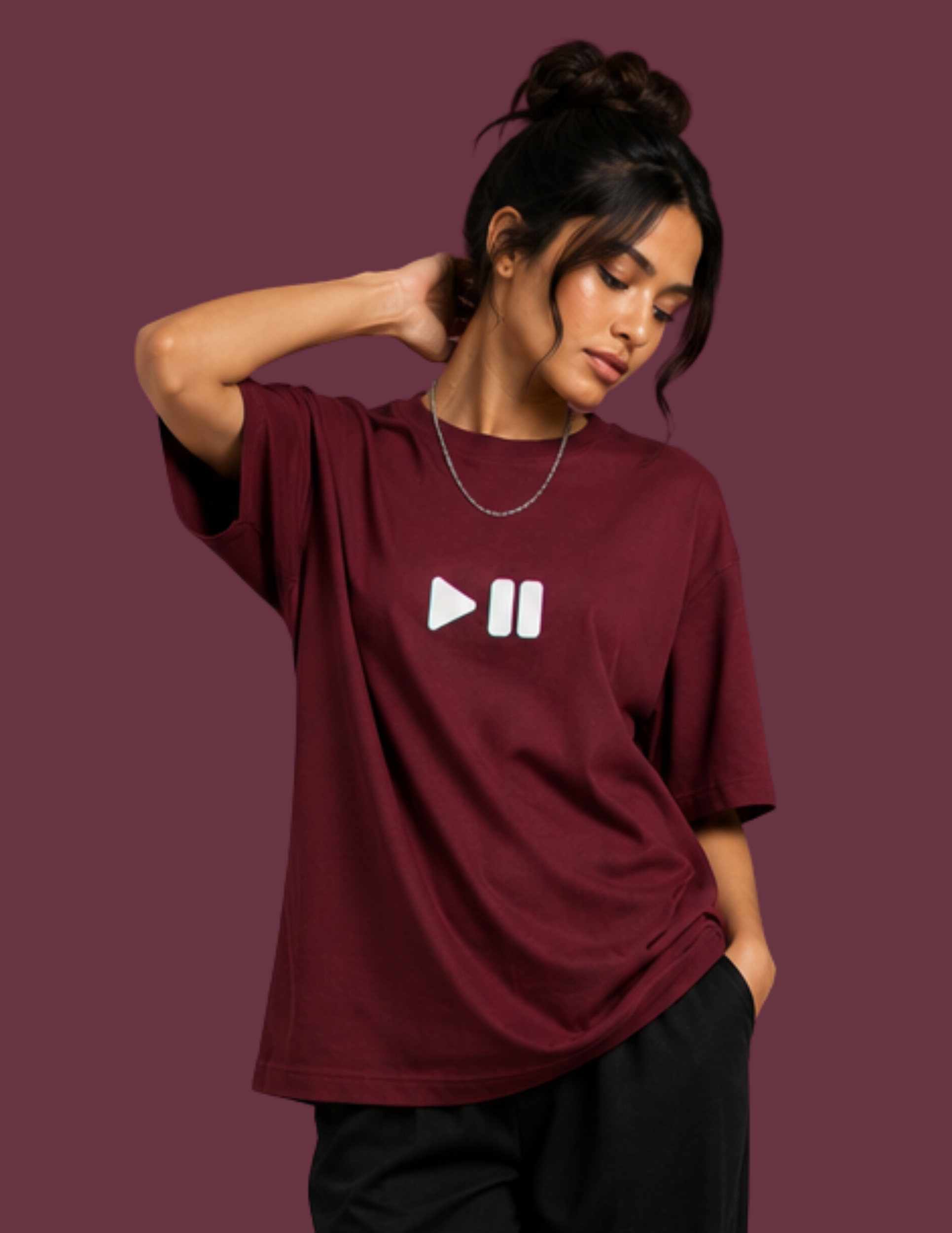 A woman wearing an oversized maroon t-shirt with a white play and pause icon printed on the chest, posed against a solid maroon background.
