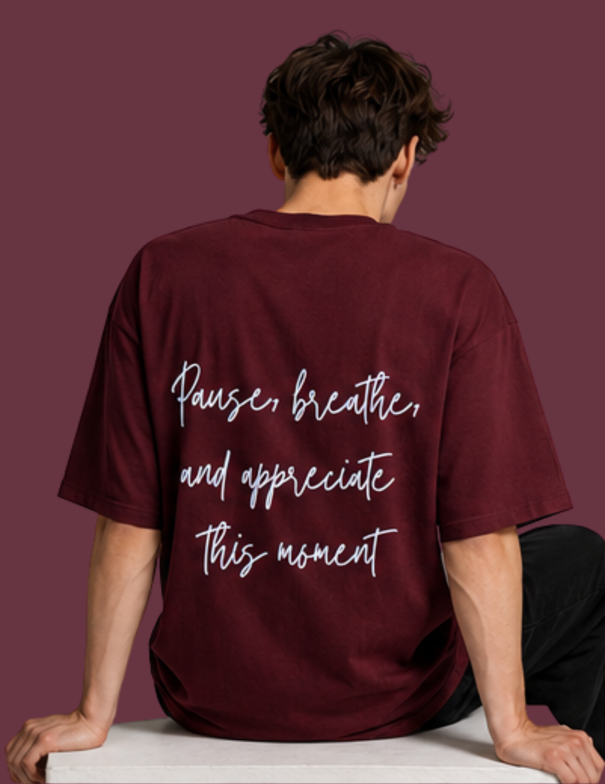 A man viewed from behind wearing a maroon t-shirt with white script text that reads 'Pause, breathe, and appreciate this moment'.