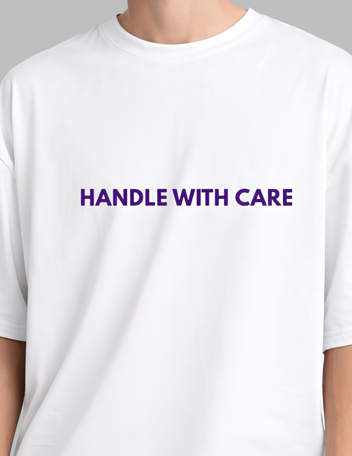 White t-shirt with 'HANDLE WITH CARE' text in purple on a gray background