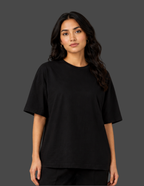 A woman modeling a plain black short-sleeve crewneck t-shirt against a solid dark gray studio background.