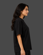 A woman in profile wearing a loose-fitting black short-sleeve t-shirt against a solid dark gray studio background.