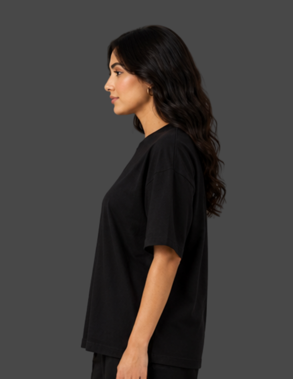 A woman shown in side profile wearing an oversized black short-sleeve t-shirt against a solid dark gray studio background.