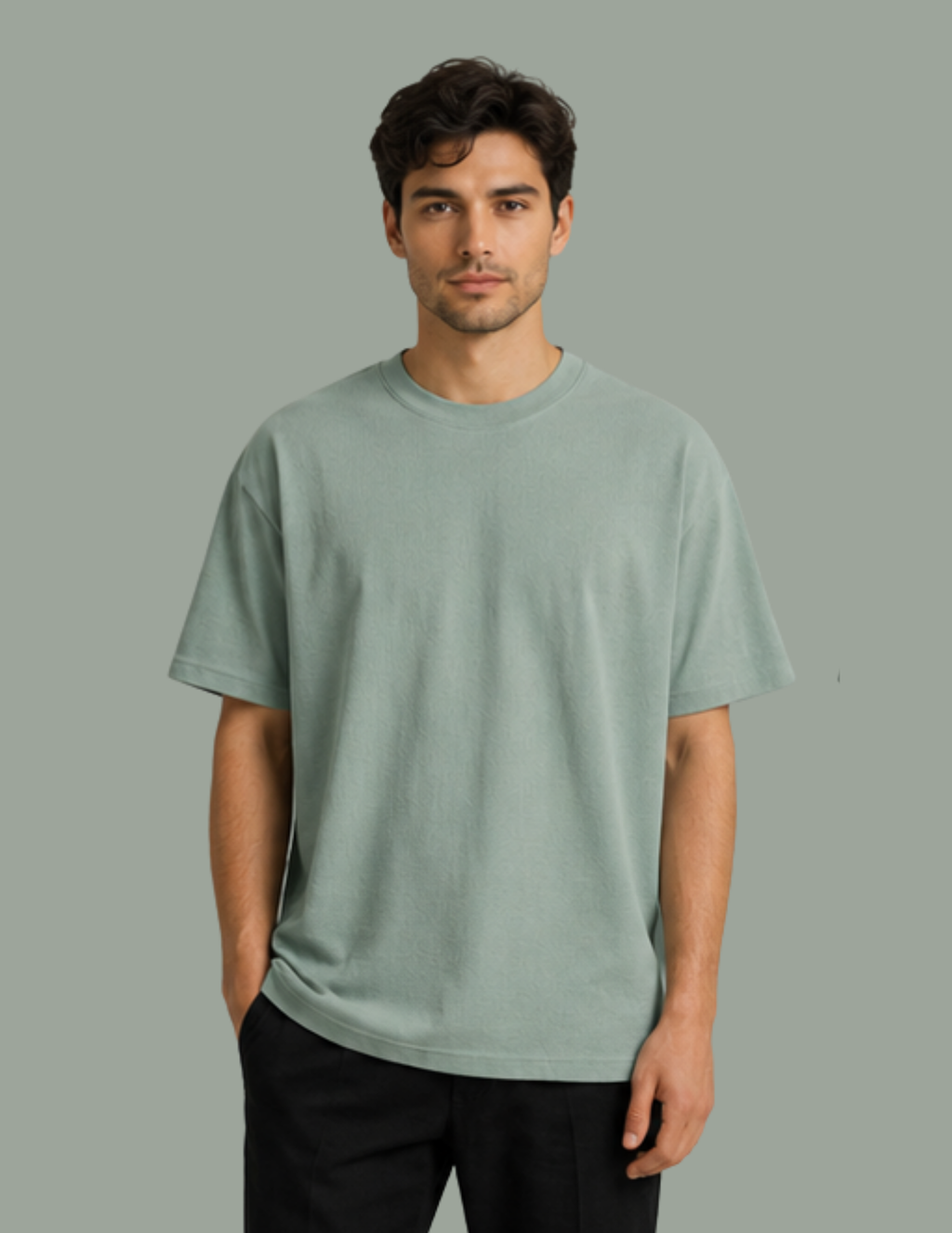 A man wearing a light sage green crewneck t-shirt and black pants, standing against a solid sage green background.