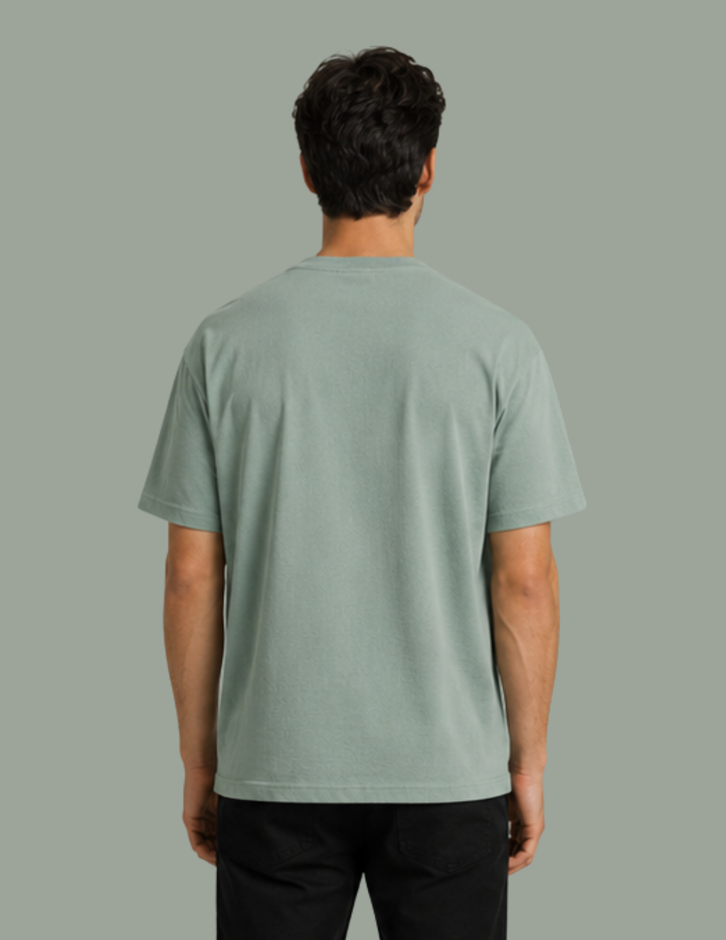 A man viewed from behind wearing a light sage green crewneck t-shirt and black pants, set against a solid sage green background.