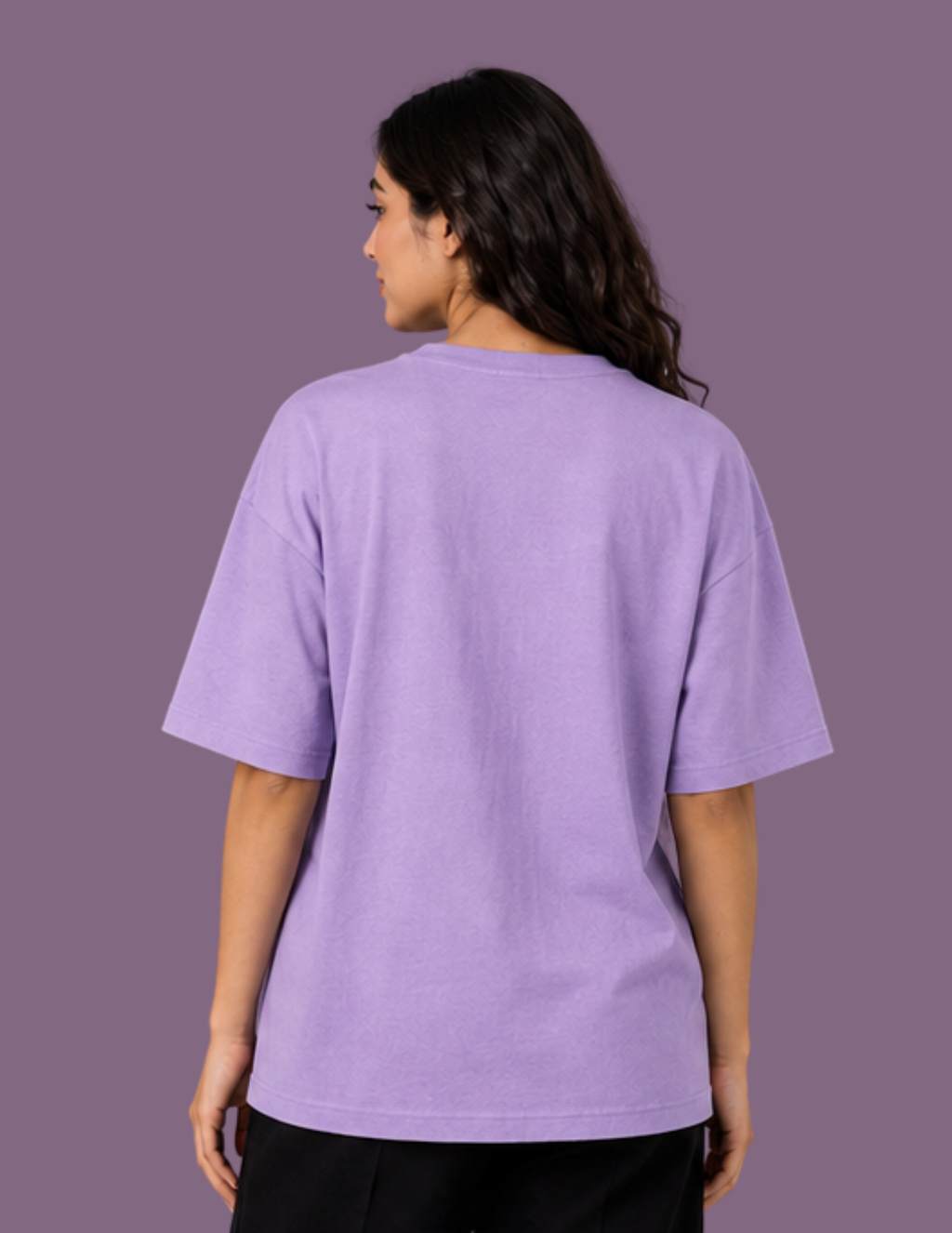 A woman viewed from the back wearing an oversized lavender-purple t-shirt and black pants, set against a solid purple studio background.