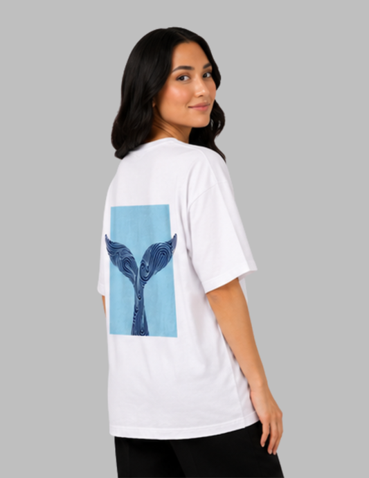 Person wearing a white t-shirt with a blue whale tail graphic on the back, standing against a gray background.