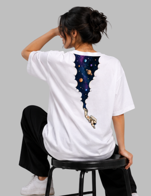 A woman wearing a white oversized T-shirt with a large back graphic of a space-themed bat silhouette and astronaut, seated on a black stool against a light gray background.