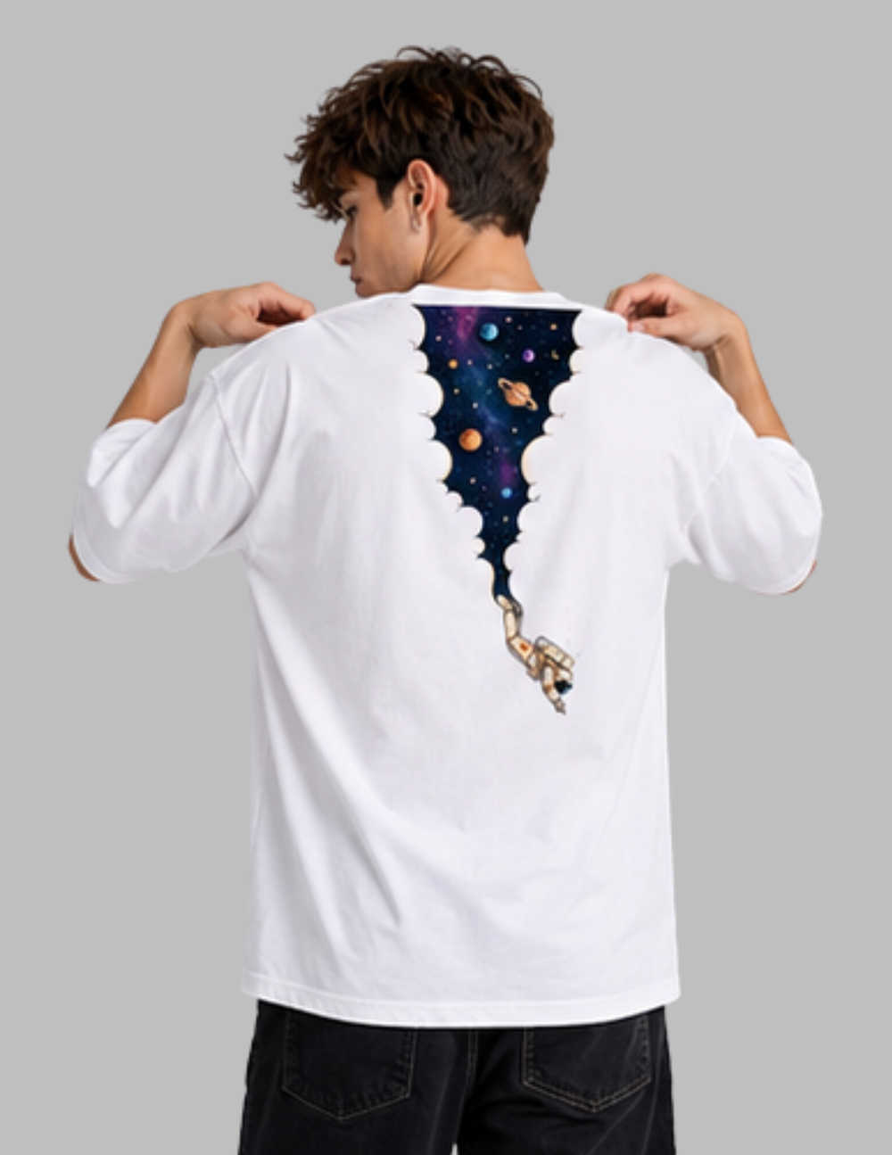A man viewed from behind wearing a white t-shirt with a graphic print of a space-themed void opening down his back, revealing a colorful galaxy and an astronaut. He is posing to show the back of the shirt against a solid gray background.