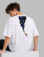 A man wearing a white oversized t-shirt, viewed from the back. The shirt features a graphic print of a cosmic space scene with planets and stars inside a cloud-like arch, with a small astronaut floating below.