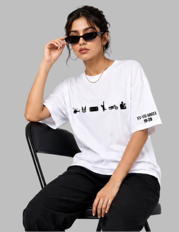 A woman wearing a white oversized T-shirt with black graphic prints and black pants, seated on a black chair against a solid gray background.