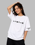 A woman wearing a white oversized graphic t-shirt with black printed icons across the chest and Roman numerals on the sleeve, posed against a solid gray background.