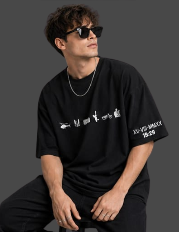 A man wearing a black oversized t-shirt with white graphic prints on the front and sleeve, paired with black pants and sunglasses, posed against a dark gray studio background.