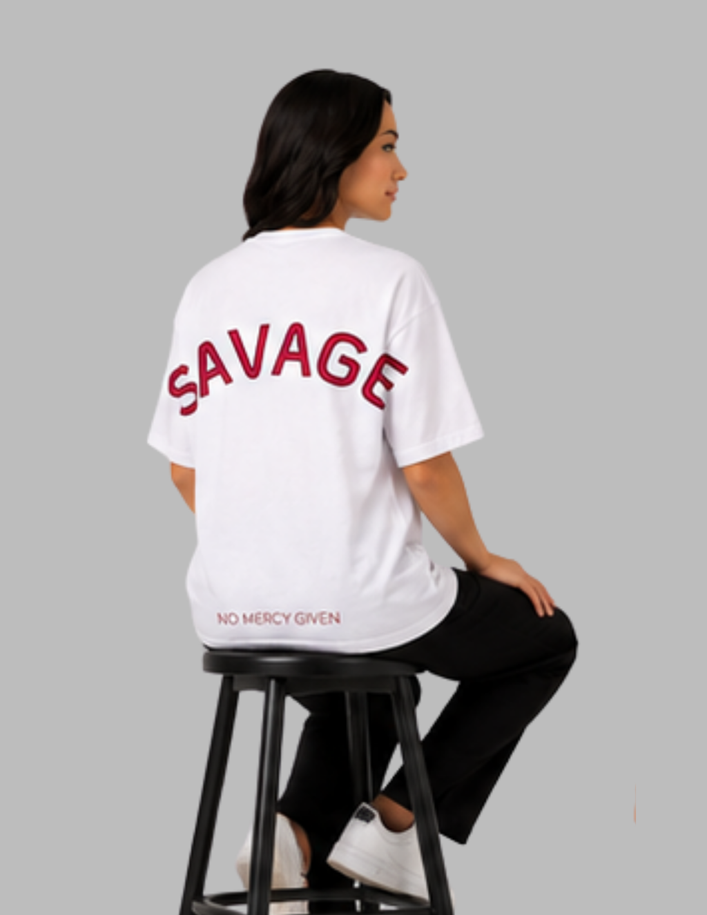 Person wearing a white t-shirt with 'SAVAGE' printed on the back, sitting on a black stool against a gray background.