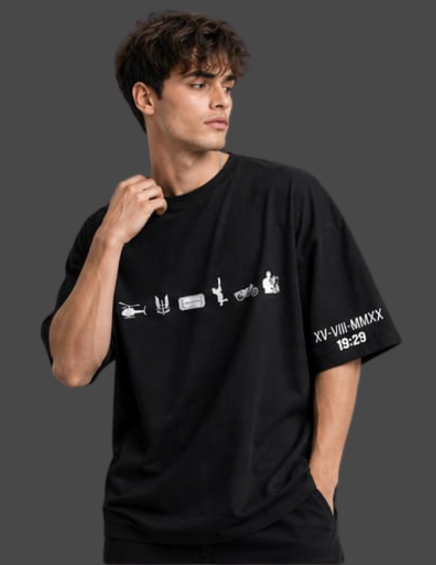 A man wearing a black oversized t-shirt with white graphic prints on the chest and sleeve, posed against a dark gray studio background.
