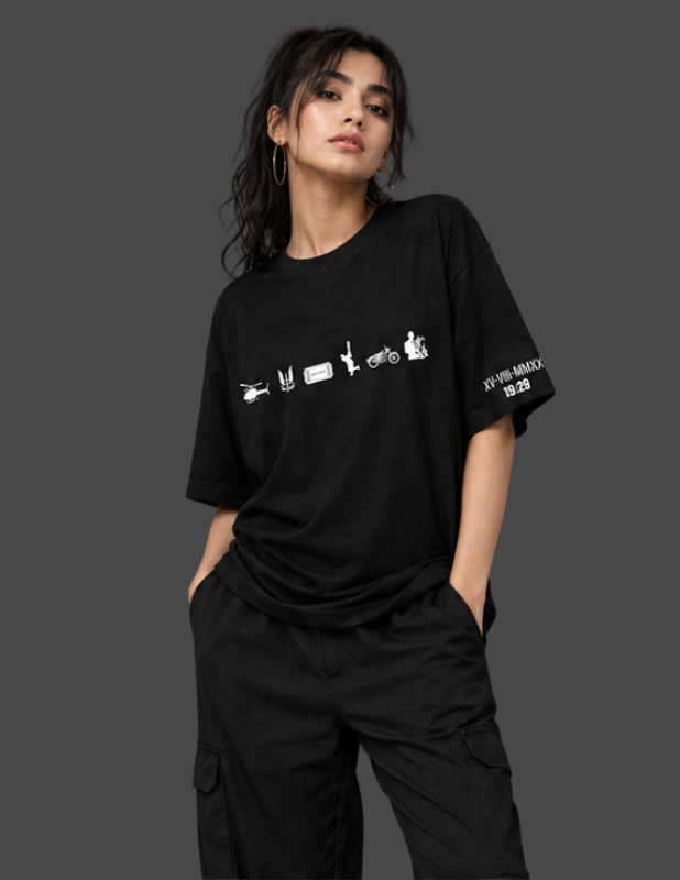 A woman modeling an oversized black t-shirt with white graphic prints on the front and sleeve, paired with black cargo pants, set against a solid dark gray background.