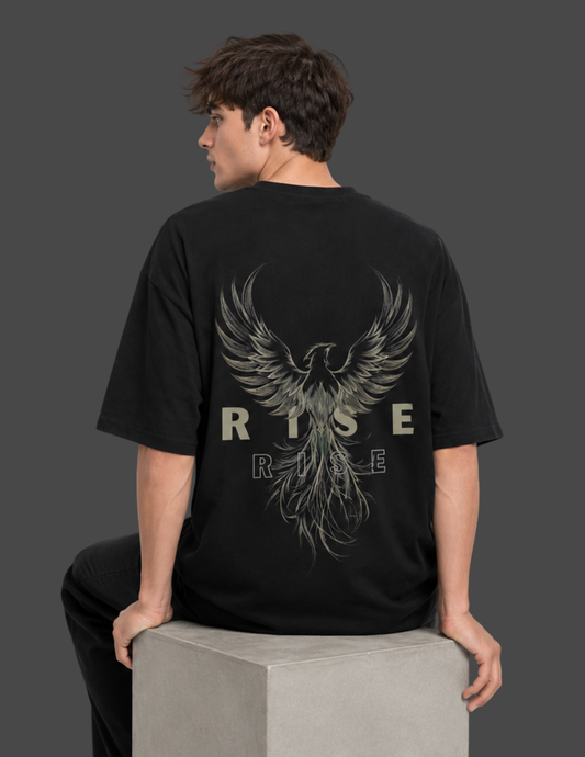 A man wearing a black t-shirt with a large graphic of a bird and the text 'RISE' on the back, sitting on a gray block against a dark gray background.