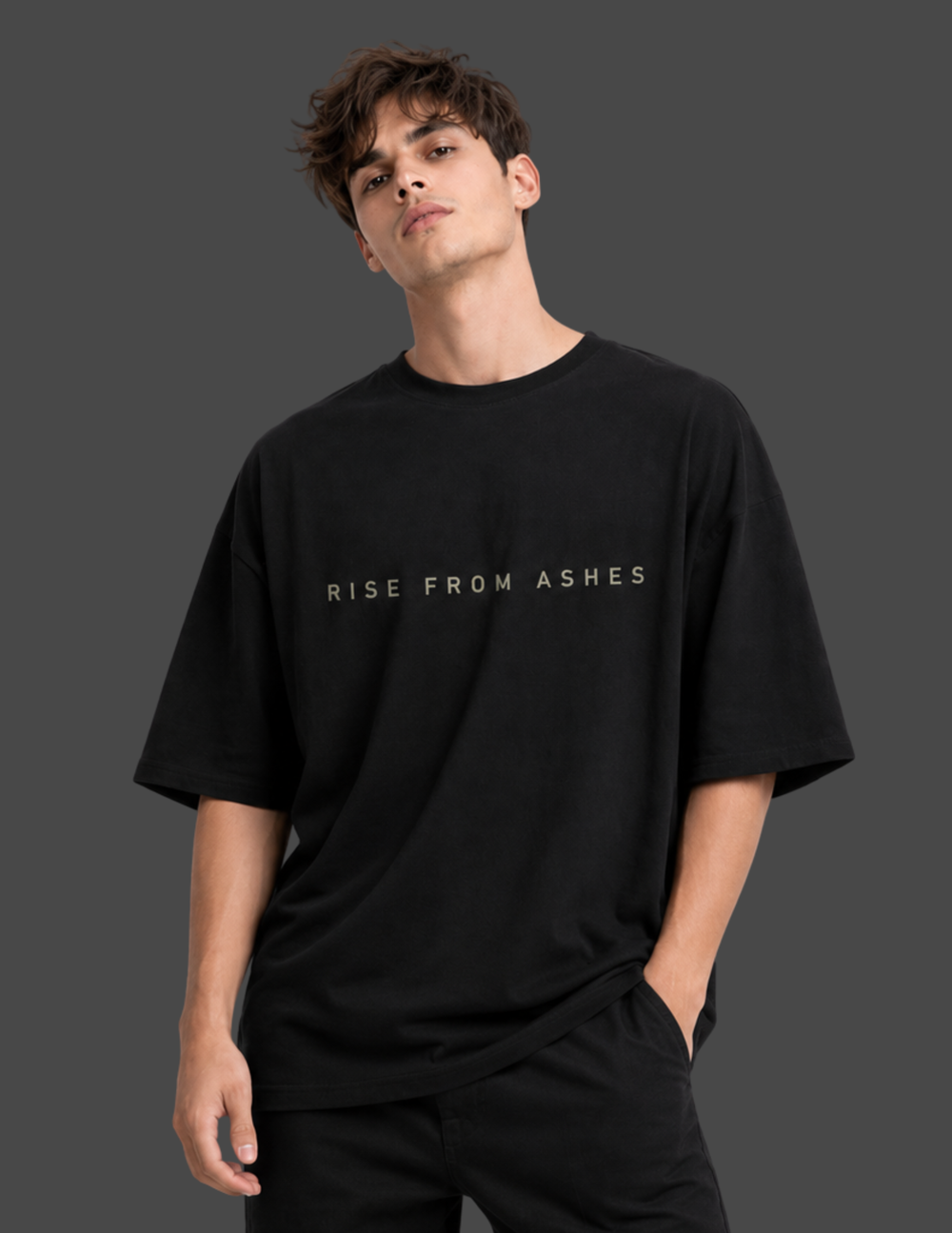 A man wearing a black oversized t-shirt with the text 'RISE FROM ASHES' printed in white across the chest, set against a dark gray studio background.