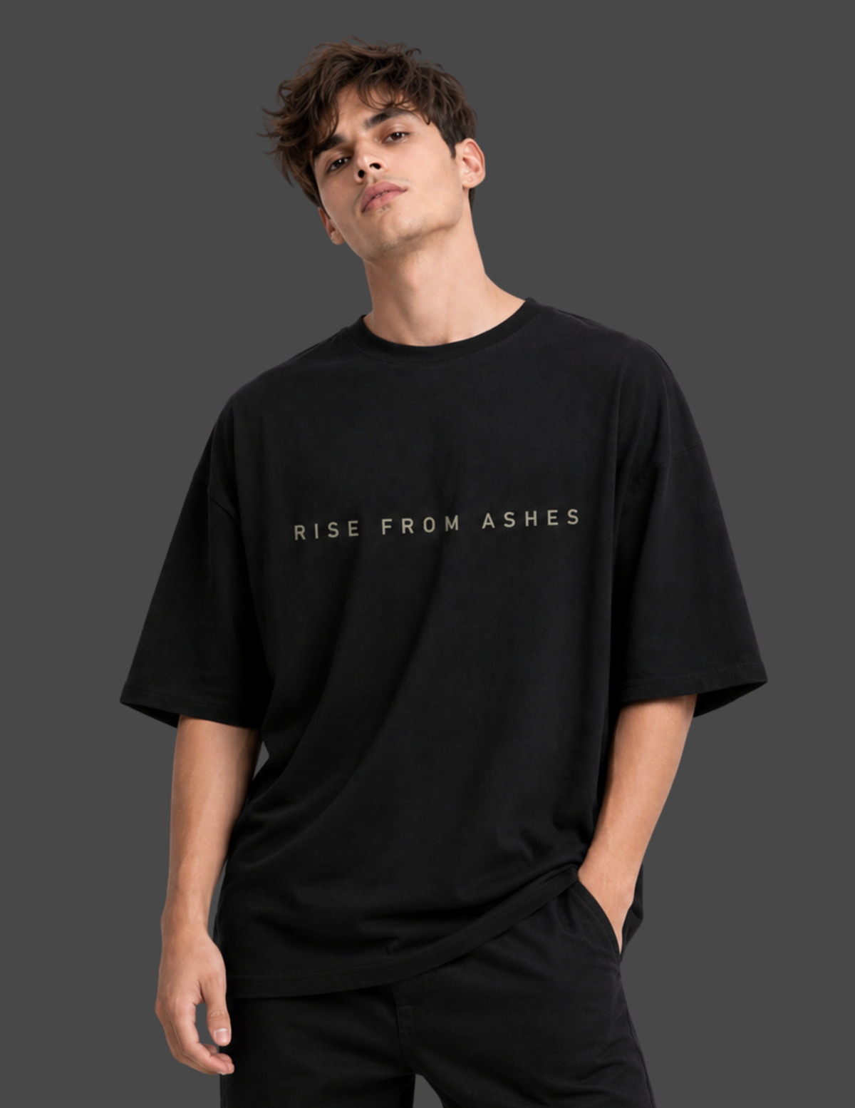 A man wearing a black oversized t-shirt with the text 'RISE FROM ASHES' printed in white across the chest, set against a dark gray studio background.
