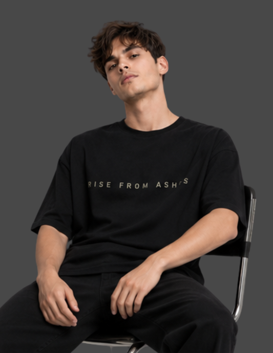A man wearing a black crewneck t-shirt with the text 'RISE FROM ASH'S' printed in a light beige color across the chest, seated on a chair against a dark gray background.