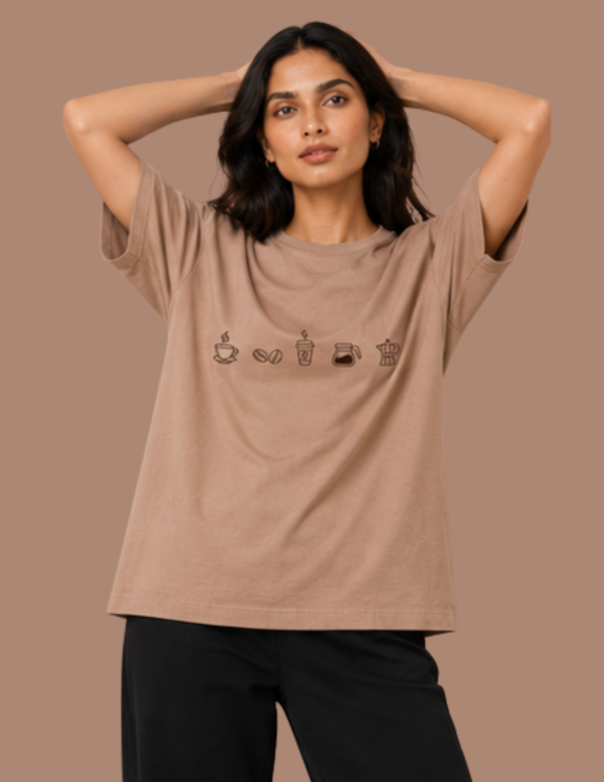 A woman modeling a taupe-brown short-sleeve t-shirt with a row of small coffee-themed icons printed across the chest, paired with black pants, set against a solid taupe background.