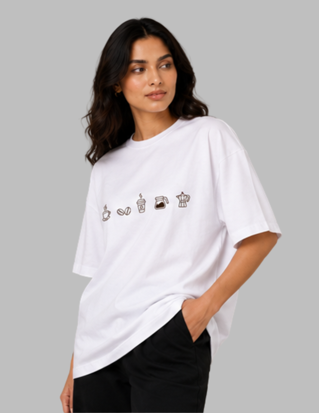A woman wearing an oversized white t-shirt with a row of small coffee-themed illustrations across the chest, paired with black pants, set against a solid gray background.