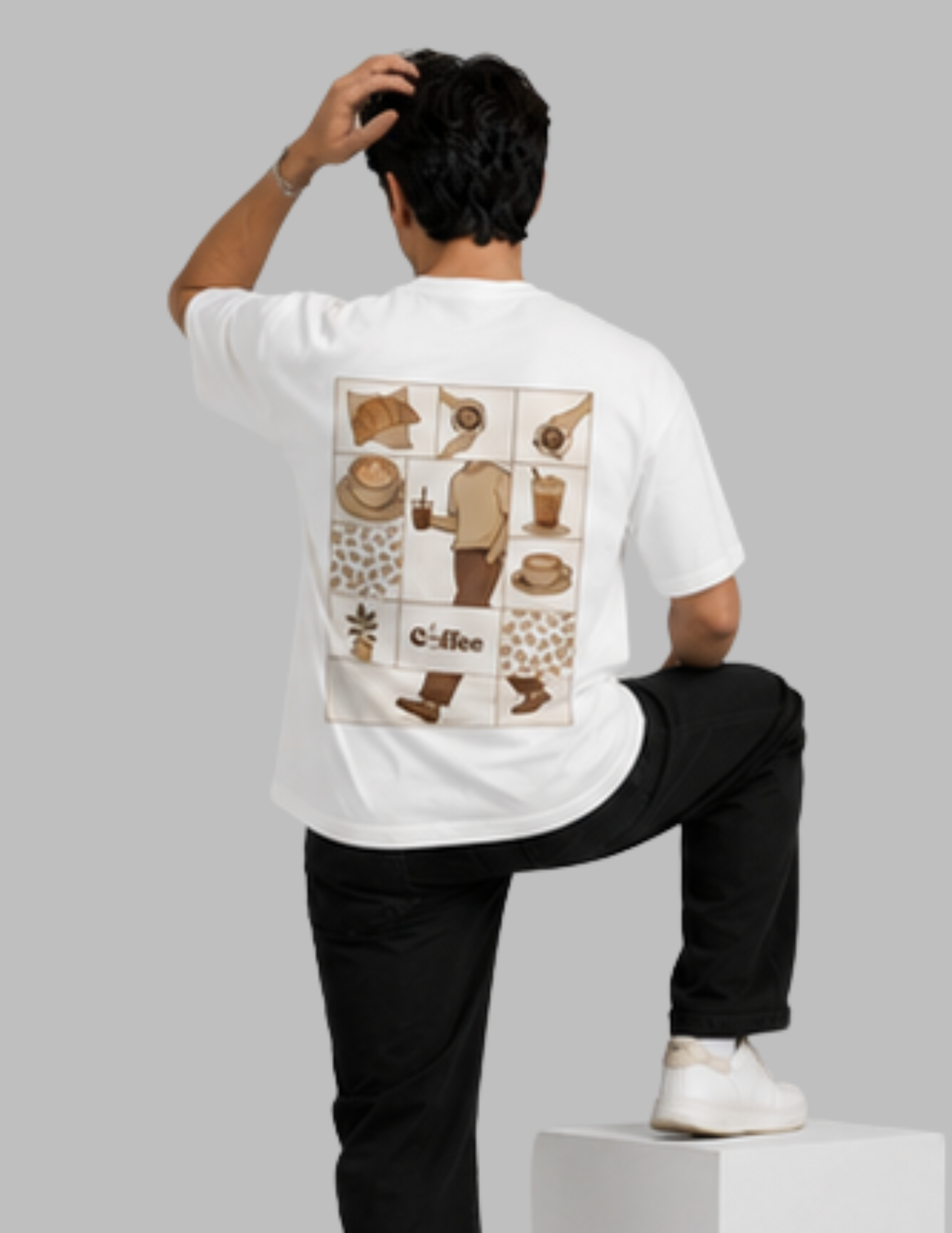 A man shown from the back wearing a white t-shirt with a large coffee-themed graphic print on the back, paired with black pants and white sneakers, standing on a white block against a solid gray background.
