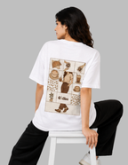 A woman wearing a white oversized T-shirt with a large vintage-style coffee-themed graphic print on the back, seated on a white stool against a solid gray background.