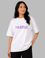 Woman wearing a white t-shirt with 'HUSTLE' in purple on a gray background