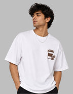 A man wearing a white short-sleeve t-shirt with a brown coffee cup and coffee bean graphic on the left chest, photographed against a solid gray background.