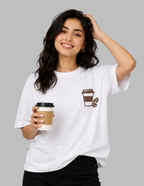 A woman wearing a white oversized T-shirt with a large vintage-style coffee-themed graphic print on the back, seated on a white stool against a solid gray background.