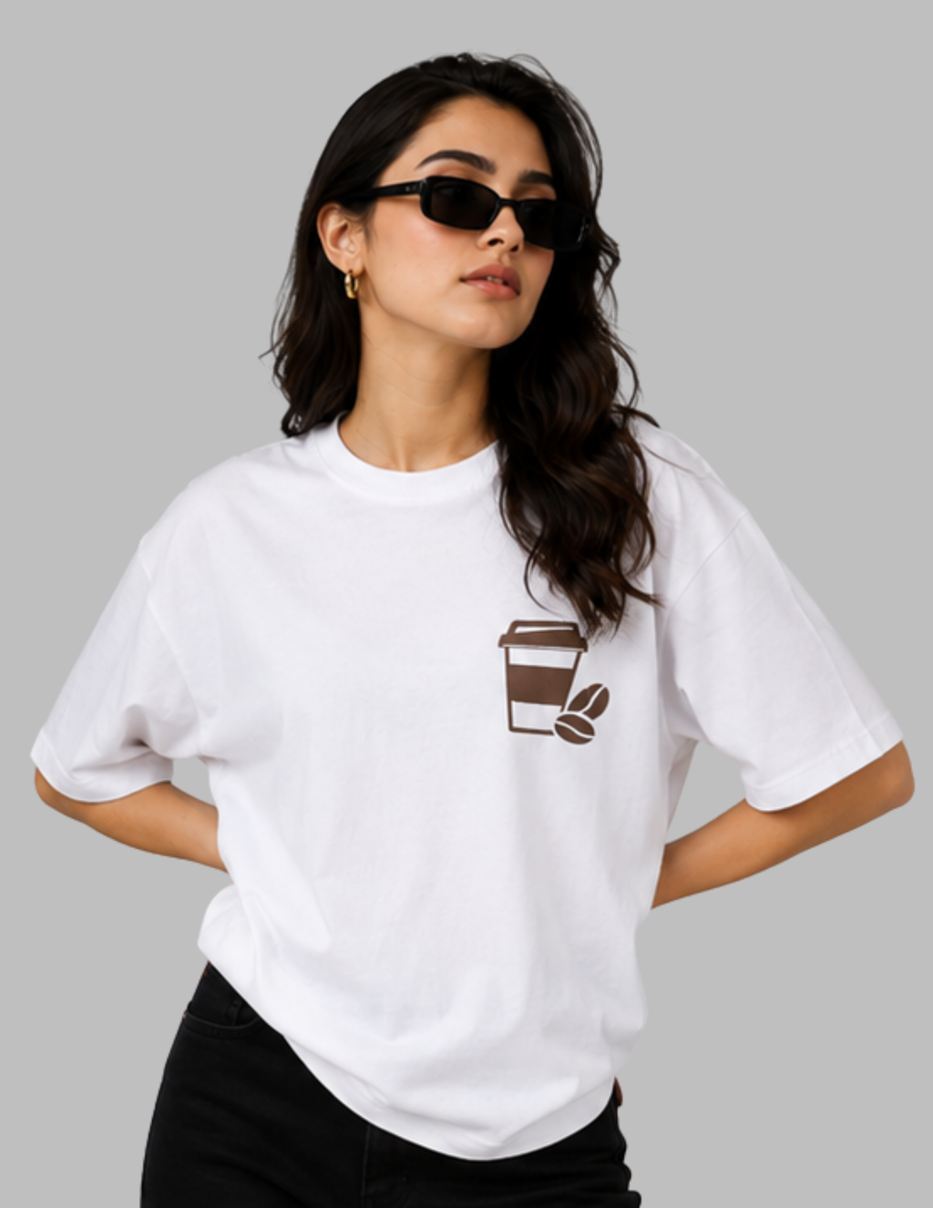 A woman wearing a white oversized T-shirt with a large vintage-style coffee-themed graphic print on the back, seated on a white stool against a solid gray background.