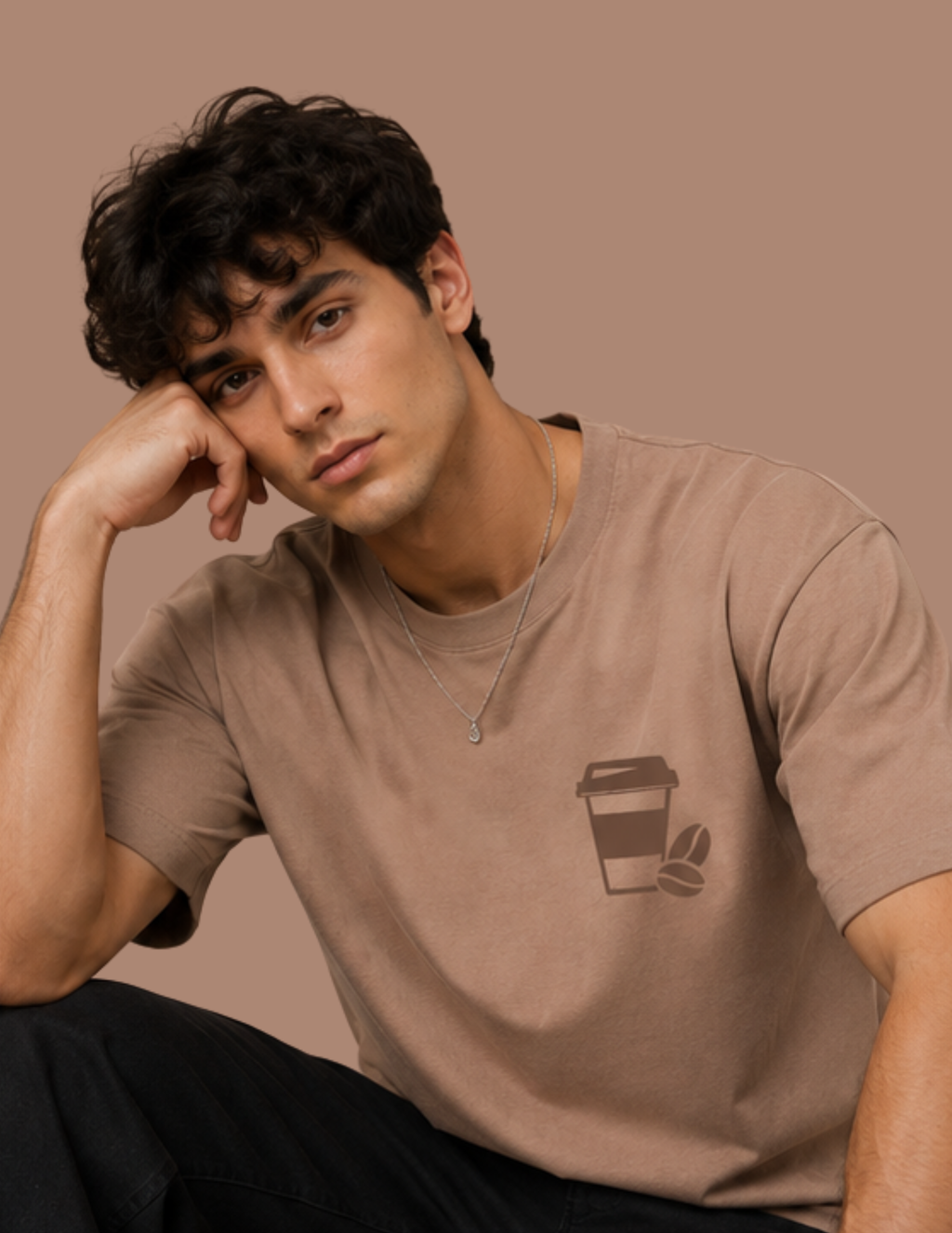 A man wearing a brown short-sleeve t-shirt with a coffee cup graphic on the left chest, posing against a solid brown background.