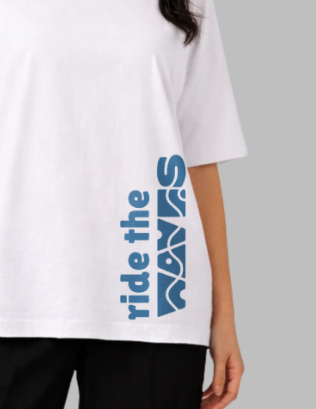 White t-shirt with blue text 'ride the waves' worn by a person on a gray background
