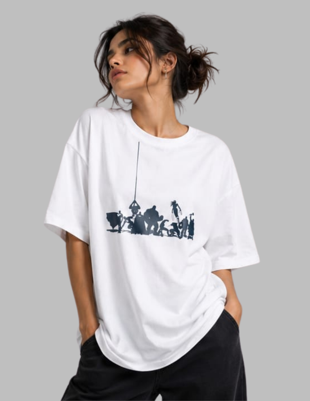 A woman wearing an oversized white t-shirt with a dark navy blue graphic print of a hanging figure, paired with black pants, set against a solid gray background.
