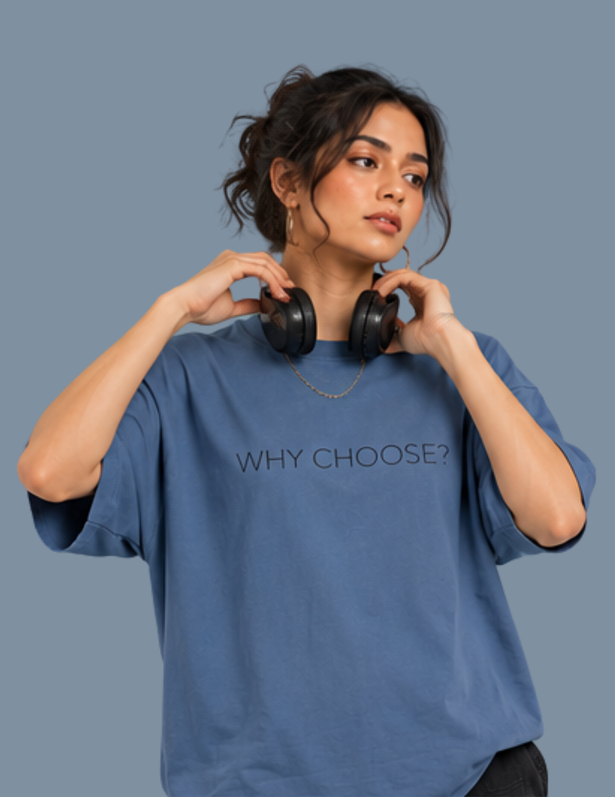 A woman wearing an oversized blue t-shirt with the text 'WHY CHOOSE?' printed on the chest, holding a pair of black headphones around her neck, against a solid slate blue background.