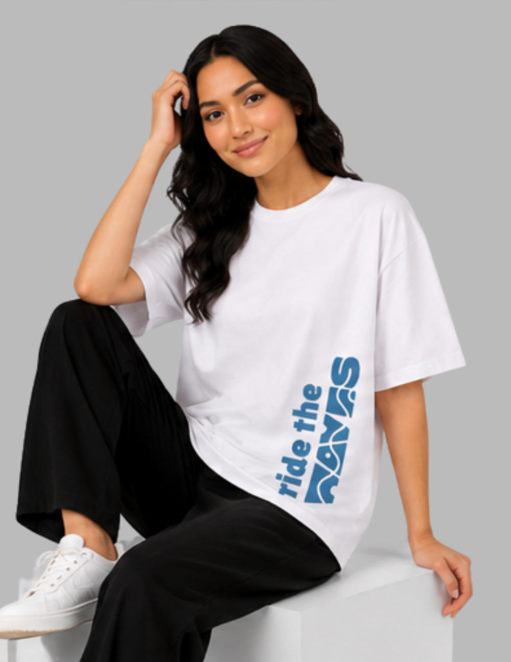 Woman wearing a white t-shirt with 'ride the waves' text, sitting on a gray background