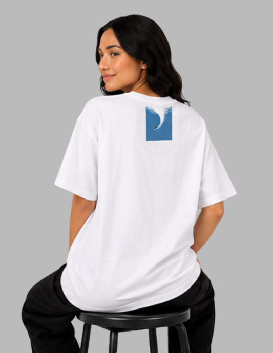 Person wearing a white t-shirt with a blue graphic on the back, sitting on a stool against a gray background