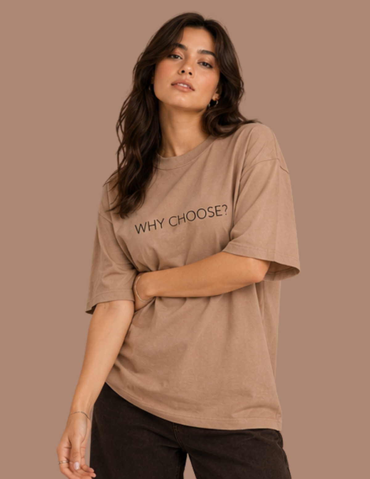 A woman modeling an oversized taupe-brown t-shirt with the text 'WHY CHOOSE?' printed in black across the chest, set against a solid taupe background.