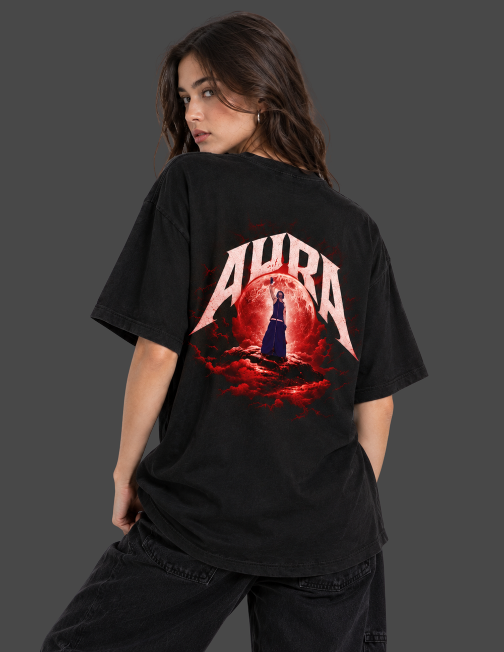 A woman wearing a black oversized graphic T-shirt, shown from the back. The shirt features a large red and white graphic with the word 'AURA' and a dark figure in front of a red circular design.