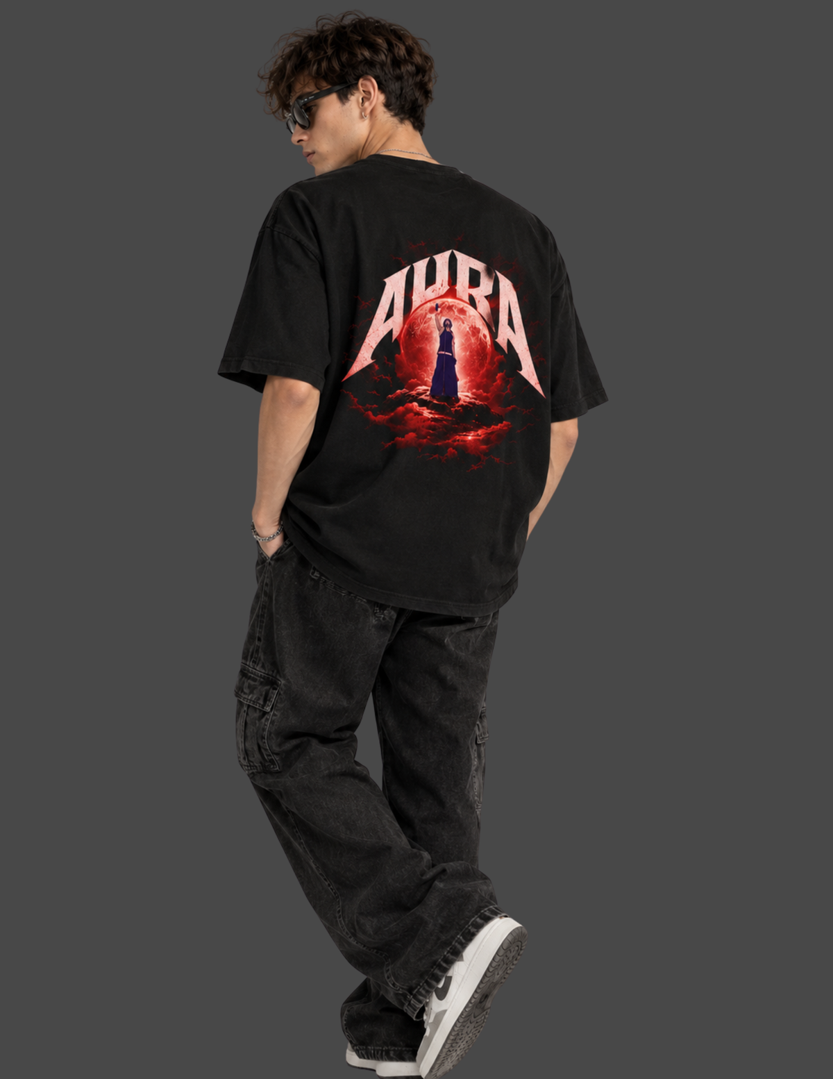 A man wearing a black t-shirt with a large red and white 'AURA' graphic on the back, paired with dark cargo pants and white sneakers, shown from behind against a solid dark gray background.