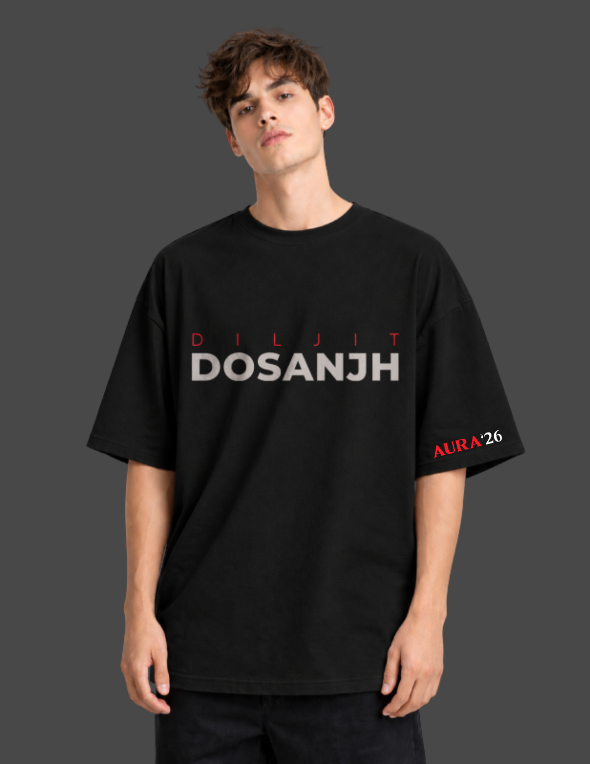 A man wearing a black oversized t-shirt with 'DILJIT DOSANJH' printed in white and red across the chest, and 'ALRA26' in red on the left sleeve, set against a dark gray background.