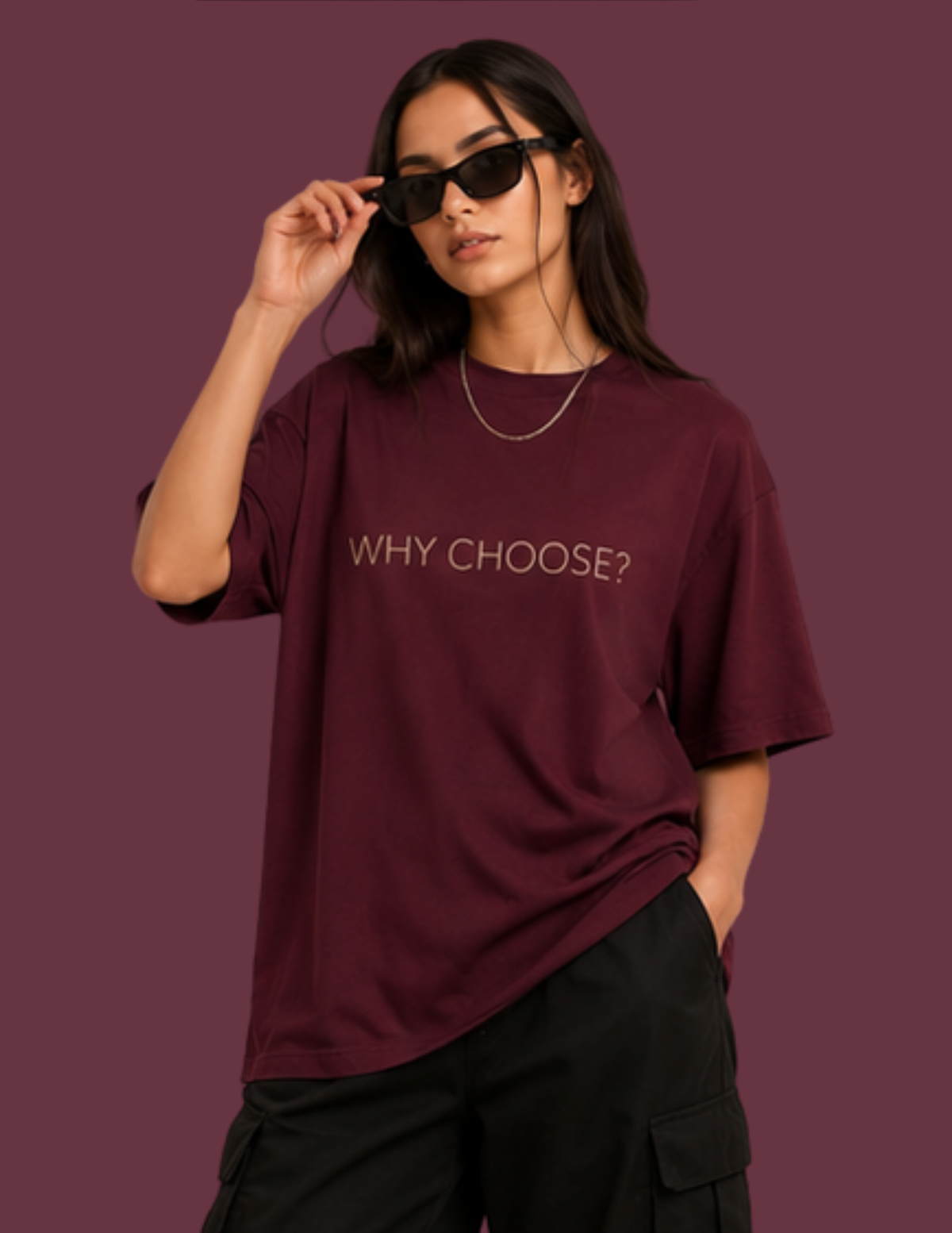 A woman wearing a maroon oversized t-shirt with the text 'WHY CHOOSE?' printed in gold on the chest, paired with black cargo pants and sunglasses, set against a solid maroon background.