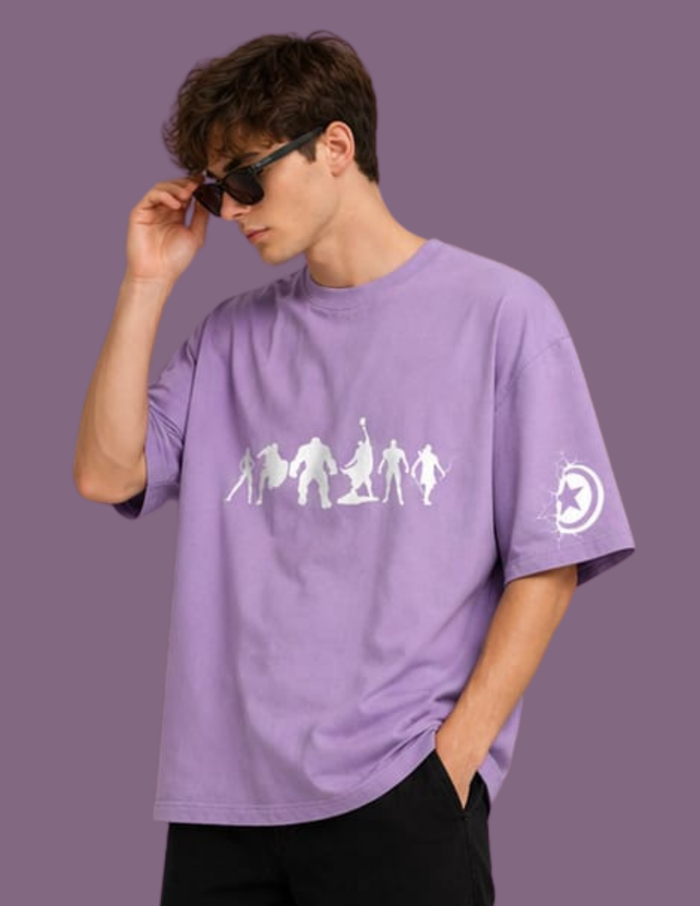 A man wearing a lavender purple oversized t-shirt with a white graphic of game characters on the chest and a moon logo on the sleeve, posed against a solid purple background.