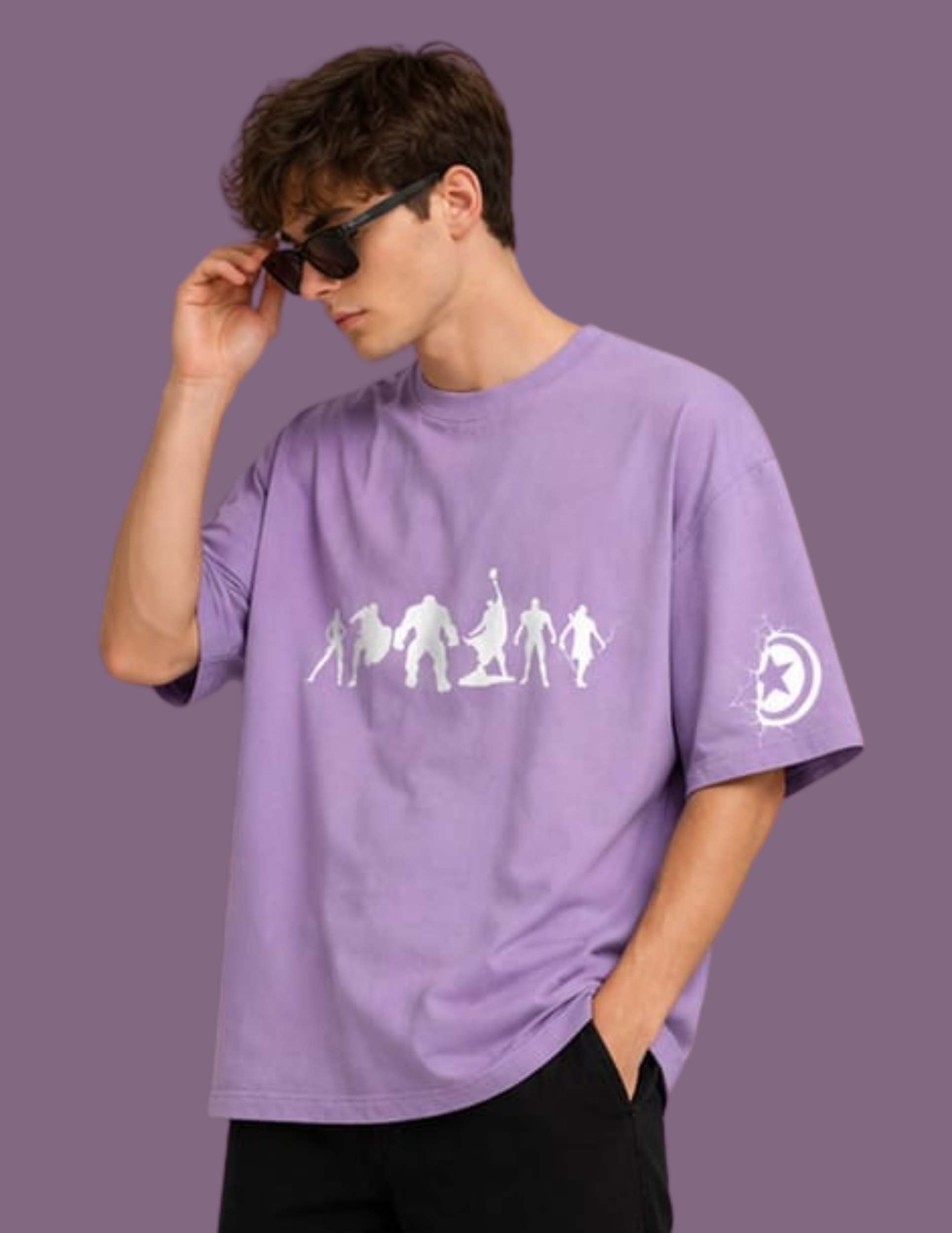 A man wearing a lavender purple oversized t-shirt with a white graphic of game characters on the chest and a moon logo on the sleeve, posed against a solid purple background.