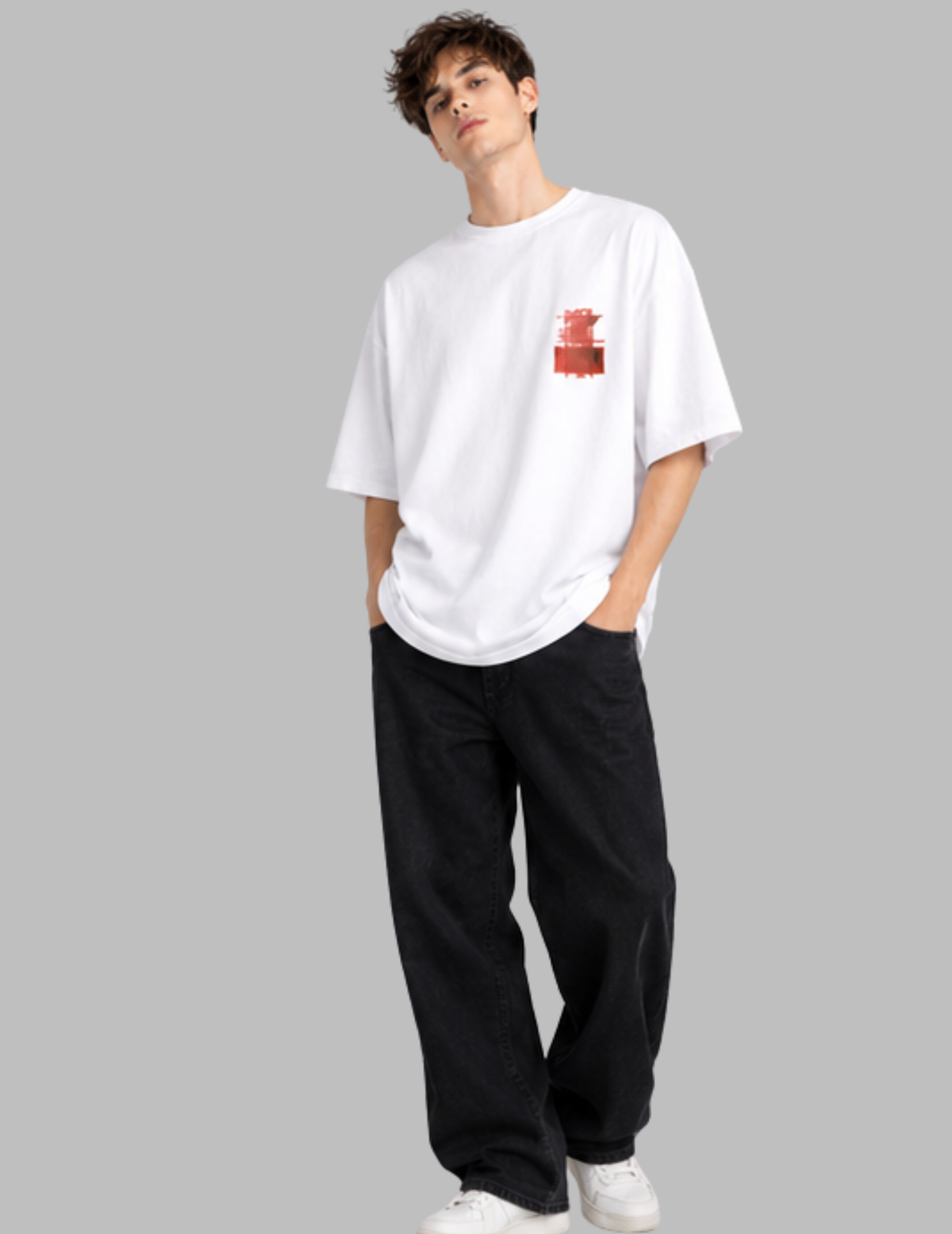 A man modeling a white short-sleeve t-shirt with a small red graphic on the left chest, paired with loose black pants and white sneakers, set against a solid gray background.
