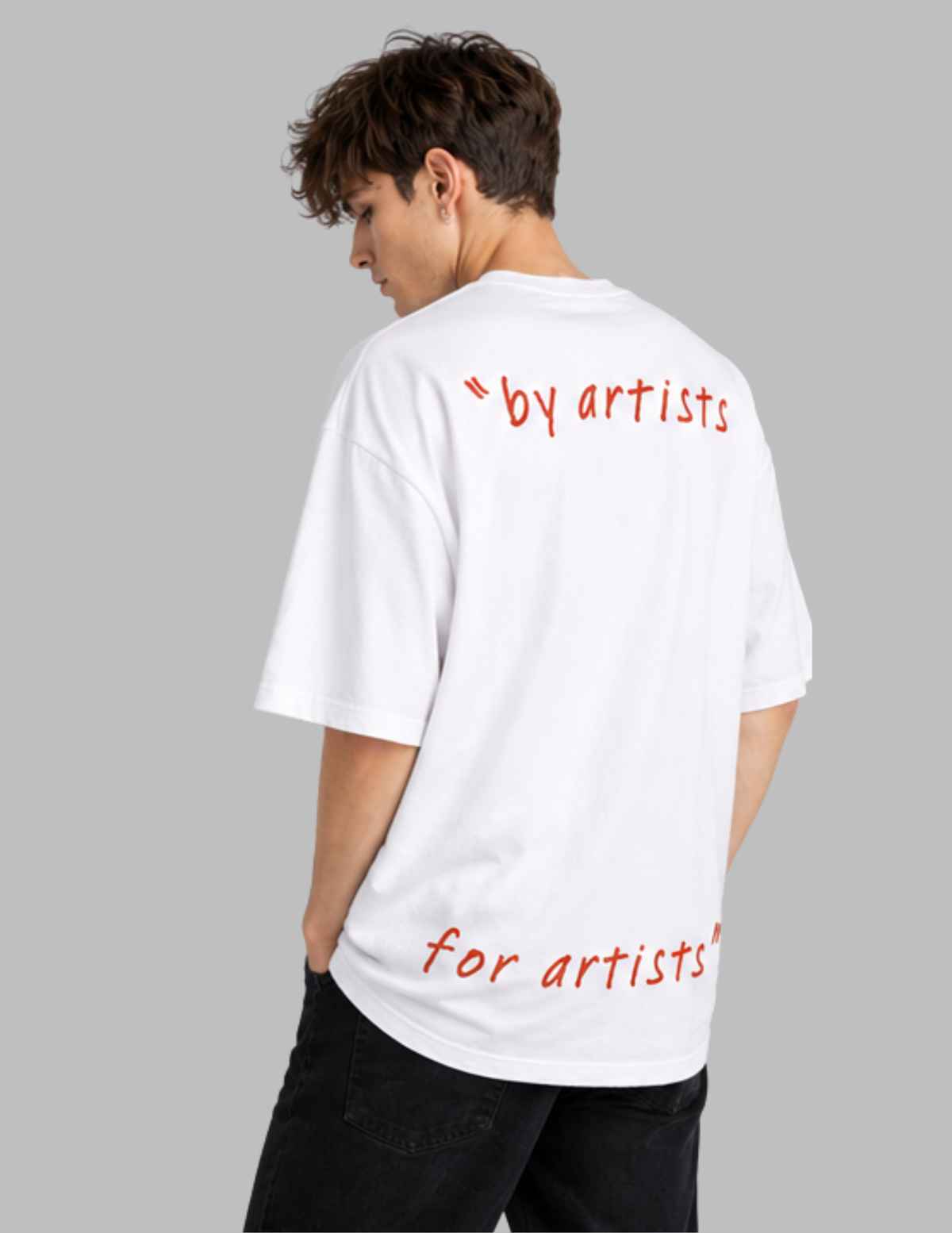 A man wearing a white oversized T-shirt from the back, featuring the red text "by artists" on the upper back and "for artists" on the lower back, against a solid gray background.