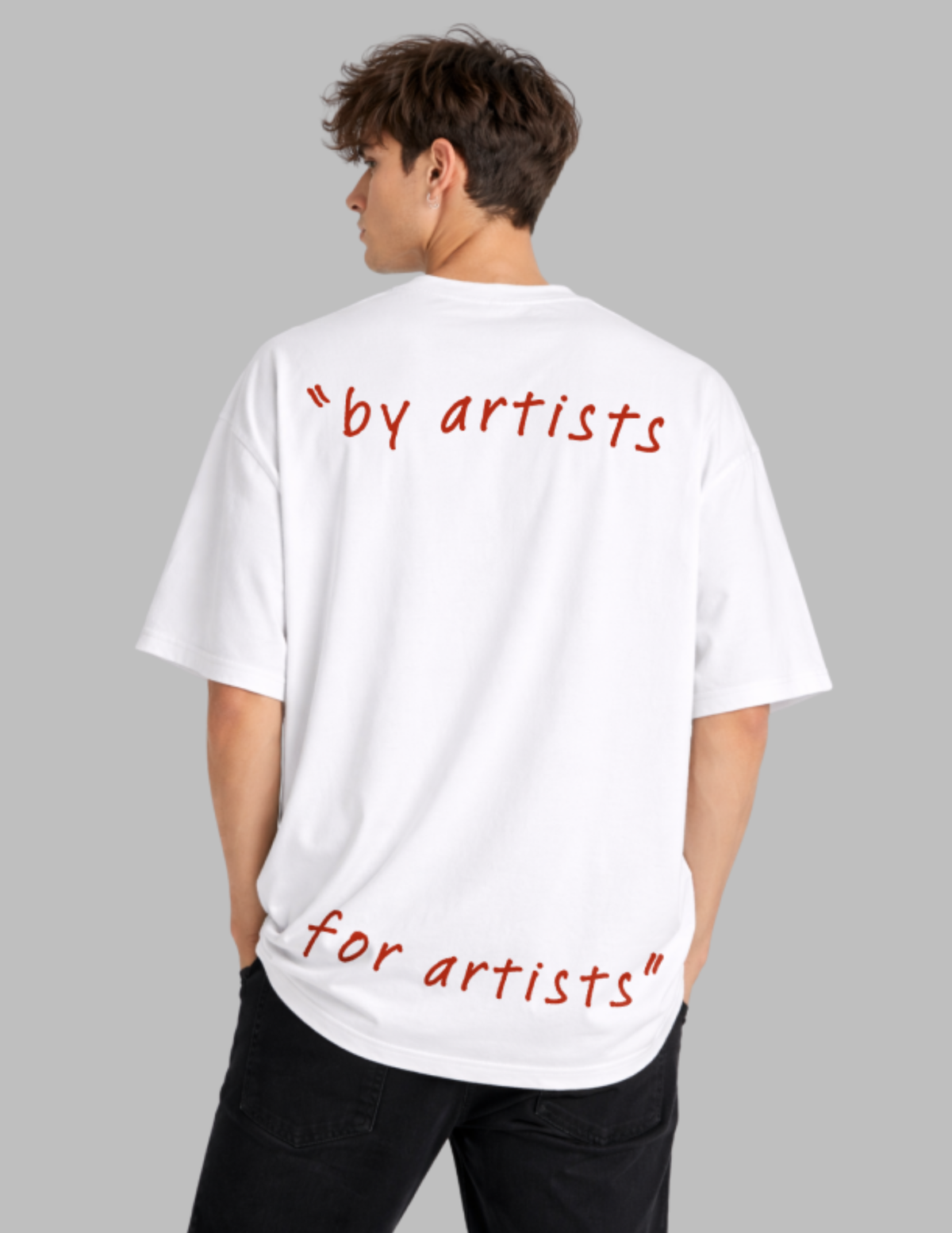 A man wearing a white oversized T-shirt from the back, featuring red handwritten-style text that reads "by artists for artists" on a solid gray background.