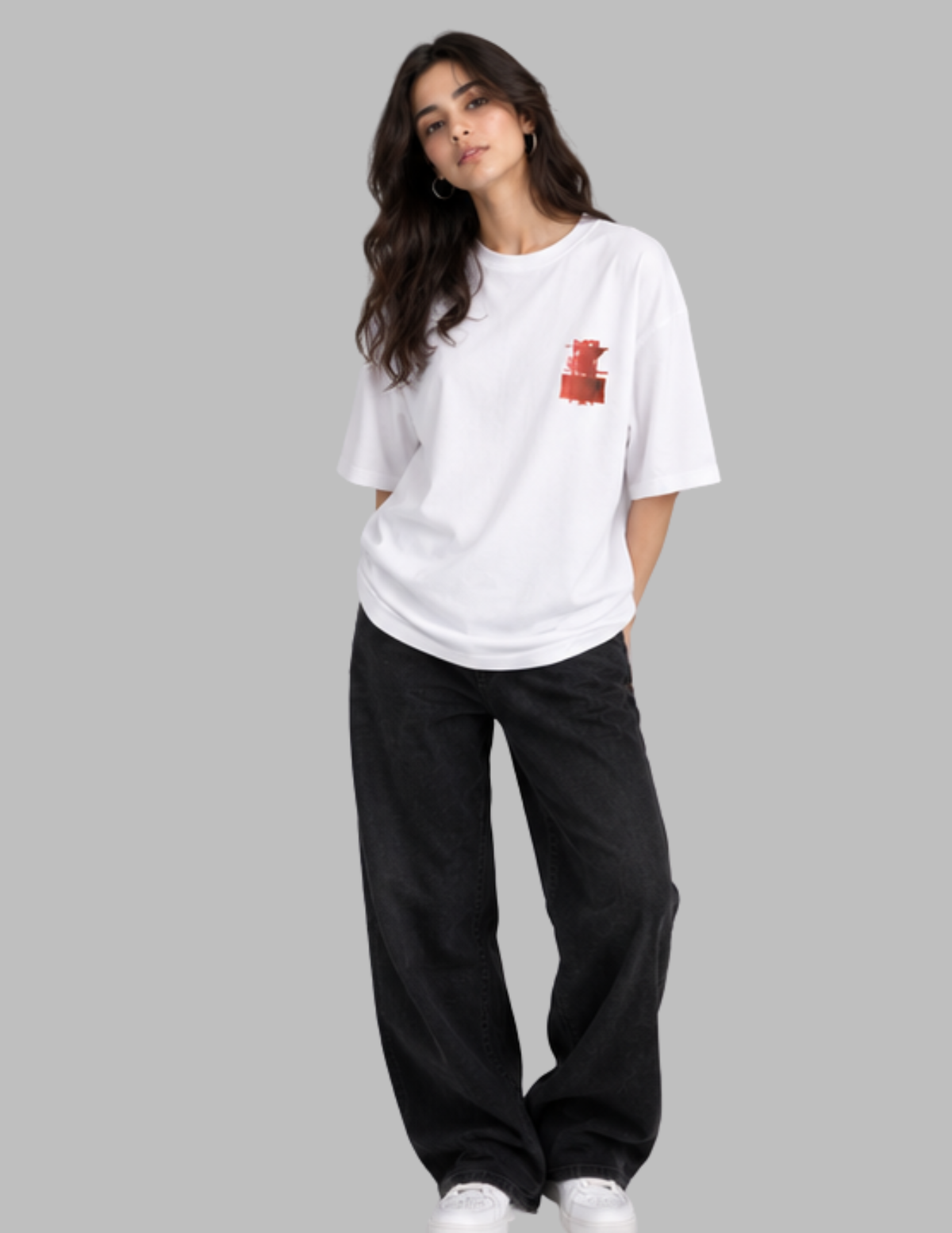 A woman modeling a white short-sleeve t-shirt with a small red graphic on the left chest, paired with black wide-leg pants and white sneakers, set against a solid gray background.